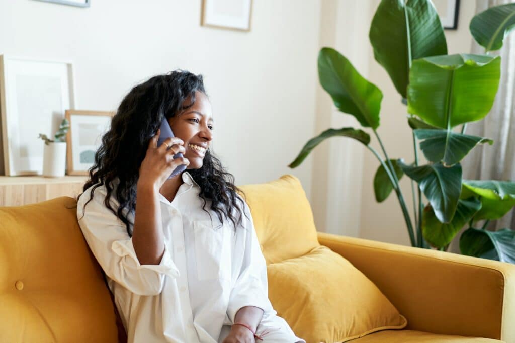 Happy African American woman on a call sitting on a sofa in living room at home
